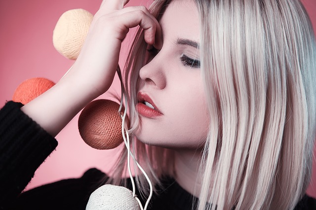Mladá žena s blond vlasmi drží svetielka pri tvári.jpg
